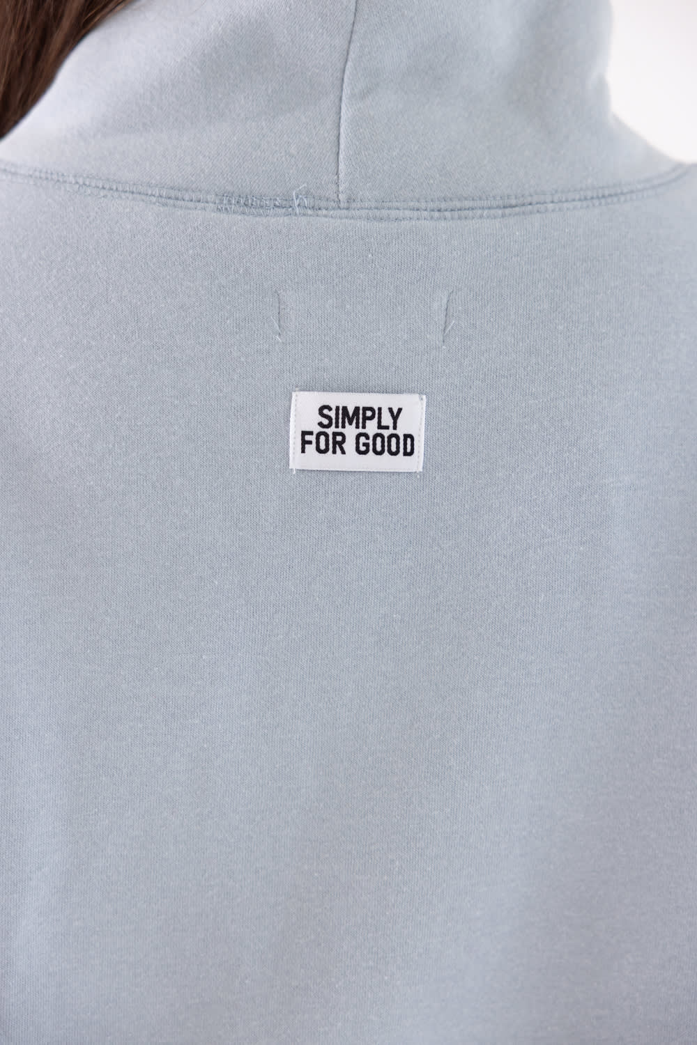 Close-up of a light blue-gray sweatshirt with a white rectangular patch reading 'SIMPLY FOR GOOD' on the upper back.