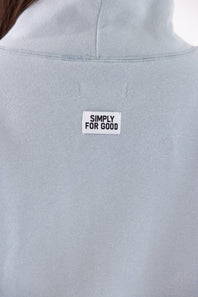 Close-up of a light blue-gray sweatshirt with a white rectangular patch reading 'SIMPLY FOR GOOD' on the upper back.