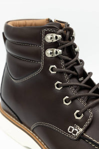 Close-up of a dark brown leather lace-up boot with silver metal eyelets and laces, showing white contrast stitching and a tan interior lining.