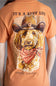 A close-up of a person wearing a peach-colored graphic t-shirt. The back of the shirt features a large illustration of a curly-haired dog wearing a cowboy hat and bandana, with the text 'IT'S A RUFF LIFE' above and 'simply souther.