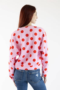 A woman shown from the back wearing a light pink crewneck sweatshirt with a bold red polka dot pattern, paired with blue jeans, against a plain white background.