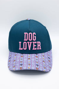 A baseball cap with a dark teal crown and a light purple patterned brim. The front of the cap features pink embroidered text reading 'DOG LOVER'.