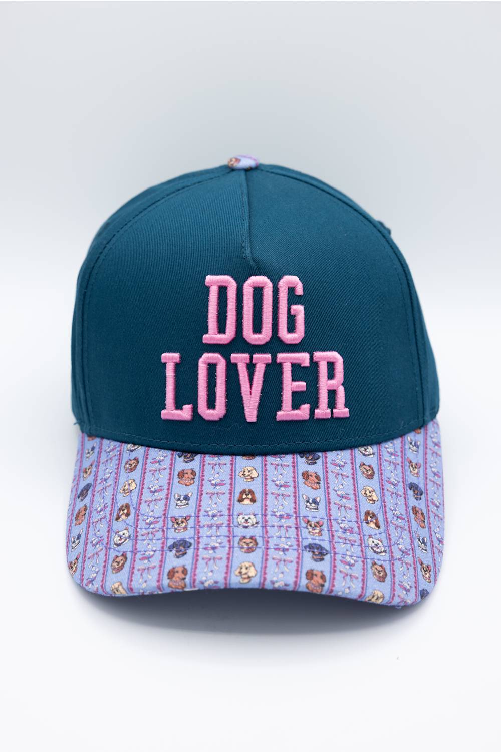 A baseball cap with a dark teal crown and a light purple patterned brim. The front of the cap features pink embroidered text reading 'DOG LOVER'.