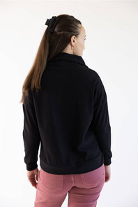 A woman shown from the back wearing a black long-sleeve collared top and pink pants, standing against a plain white background.