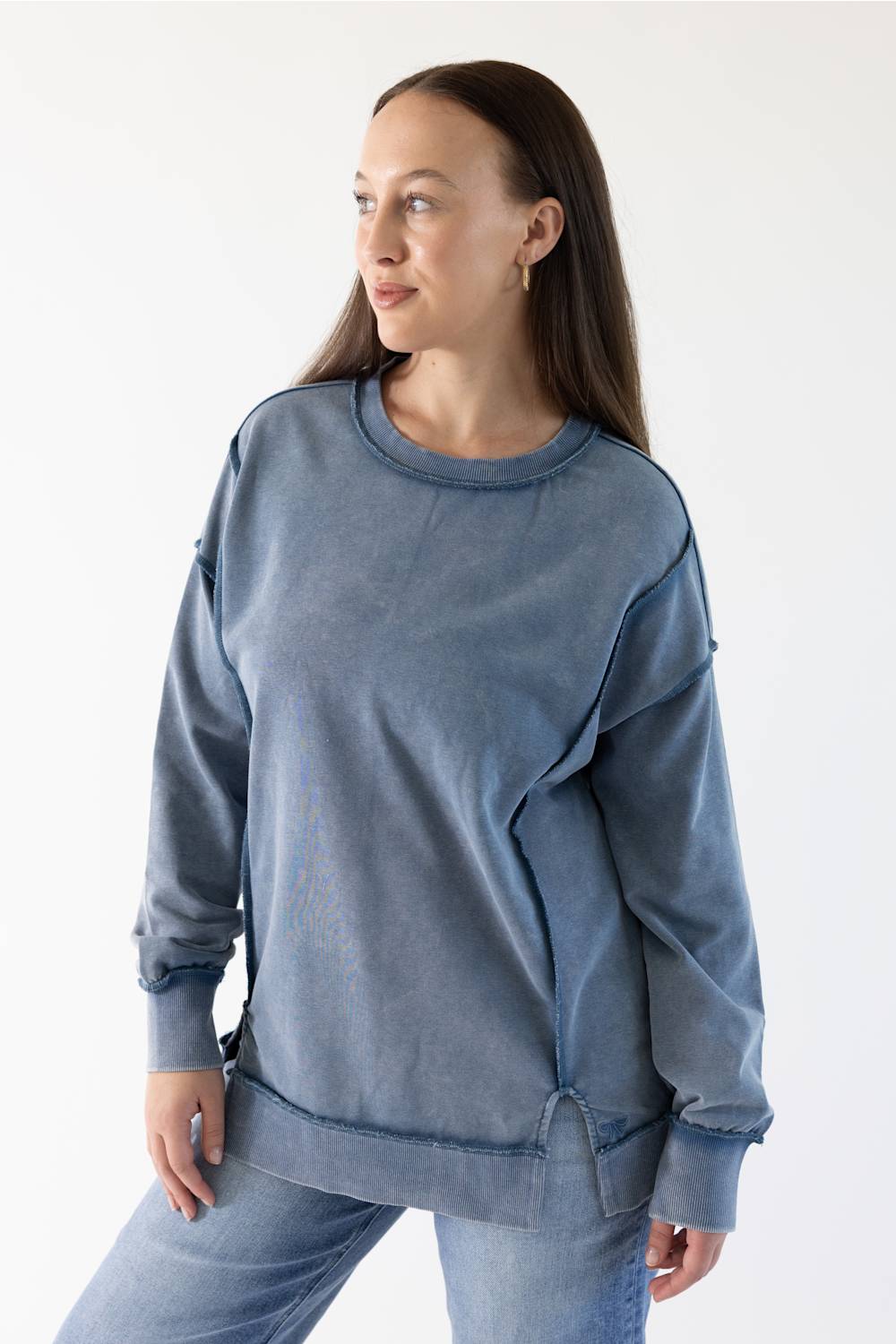 A woman wearing a washed slate blue crewneck sweatshirt and matching blue jeans, photographed against a clean white studio background.