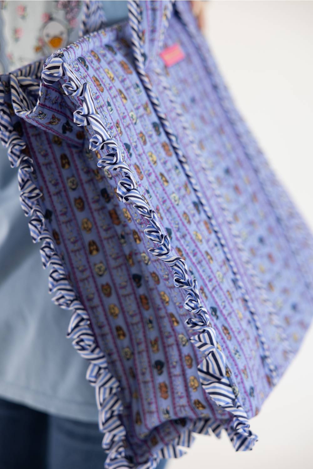 A close-up of a person holding a lavender patterned quilted bag with black and white striped ruffle trim.