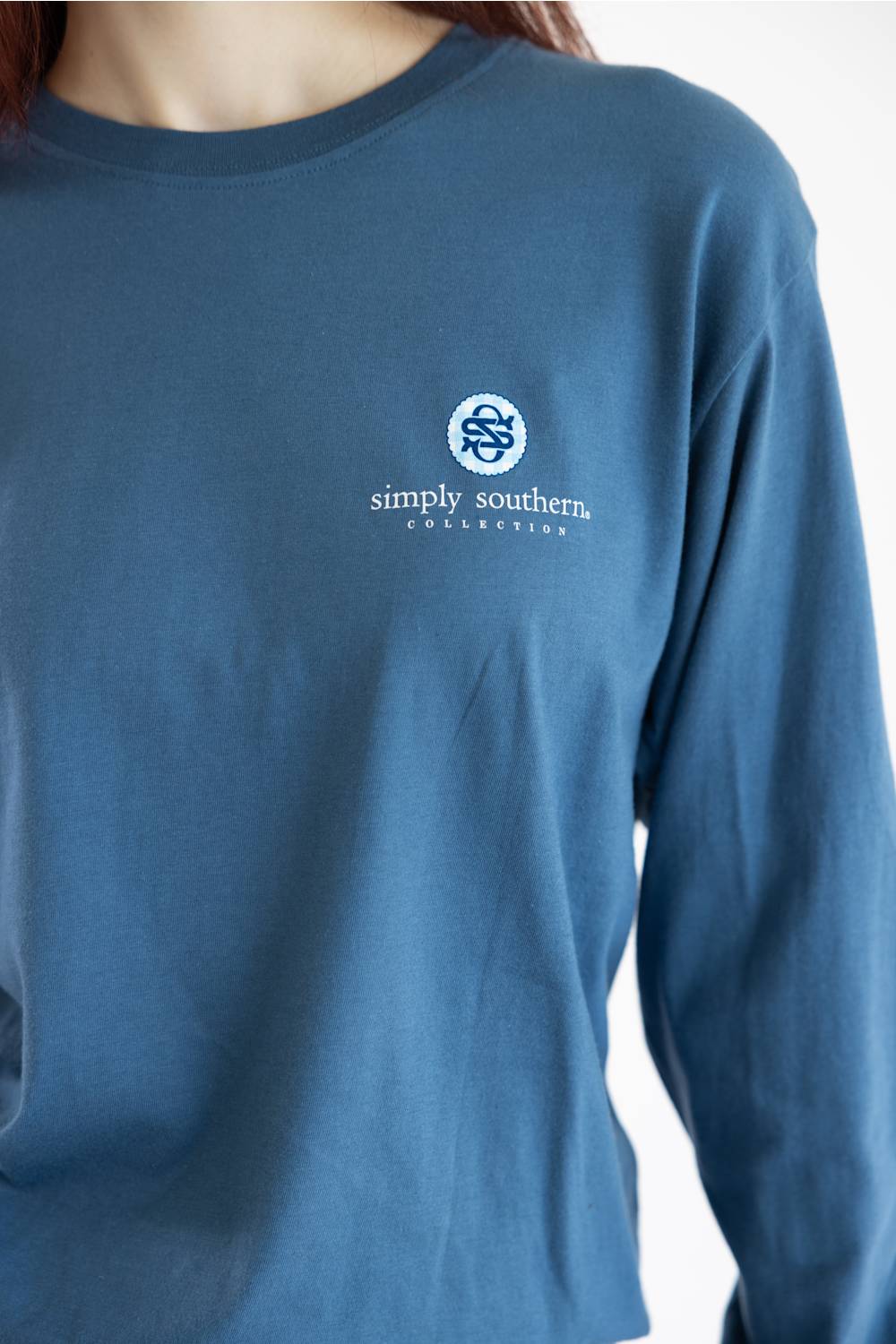 A close-up of a person wearing a slate blue long-sleeve t-shirt with a white embroidered 'simply southern foundation' logo on the left chest.