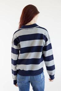 A woman viewed from behind wearing a navy blue and light gray horizontally striped long-sleeve sweater with a mock neck, paired with blue jeans, against a plain white background.