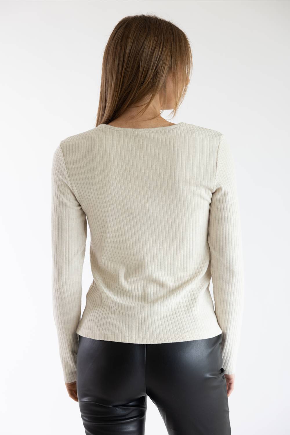 A woman viewed from the back wearing a cream ribbed knit long-sleeve top and black faux-leather pants against a plain white studio background.