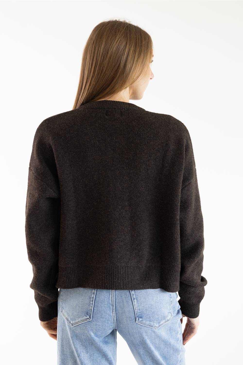 A woman viewed from behind wearing a dark brown knit sweater and light blue jeans against a plain white background.