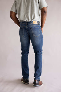 Back view of a person wearing blue jeans and a gray shirt on a plain background. The jeans are Weatherproof Vintage Slim Jeans for Men in Tidepool Tint.