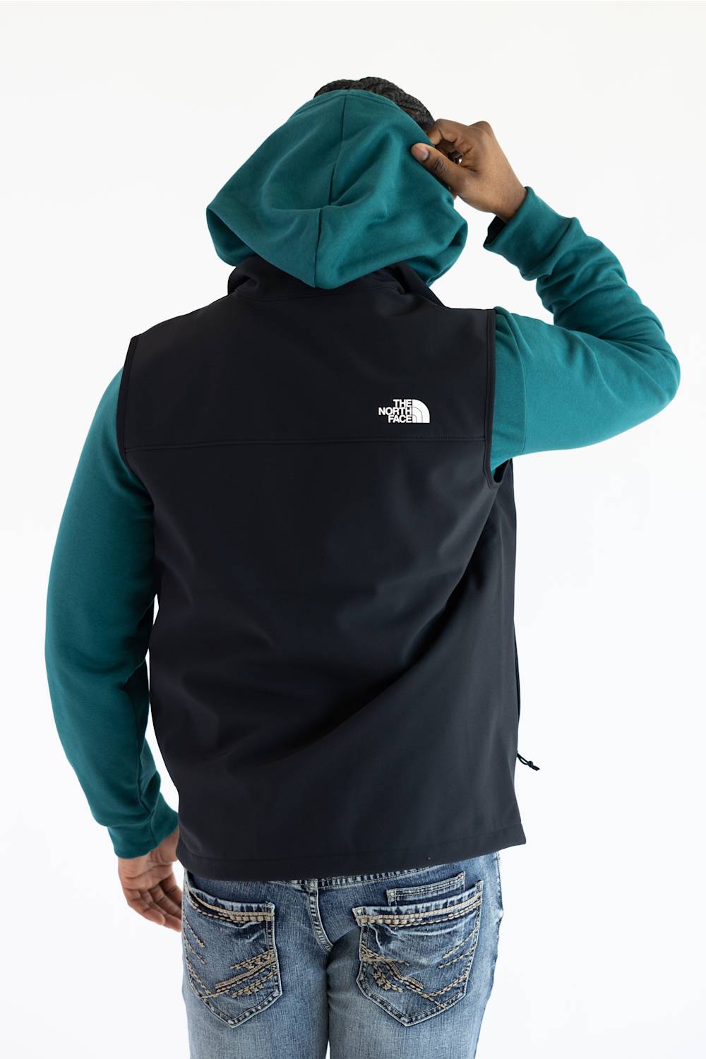 A person wearing a black vest over a teal hoodie, with The North Face logo printed in white on the upper right shoulder.