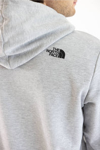 Close-up of a person wearing a light heather gray hoodie from the back, showing the black The North Face logo on the upper back.