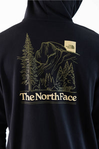 Close-up of the back of a black hoodie featuring a large gold line art graphic of a mountain and pine trees, with 'The North Face' text printed below and a small brand patch on the upper back.