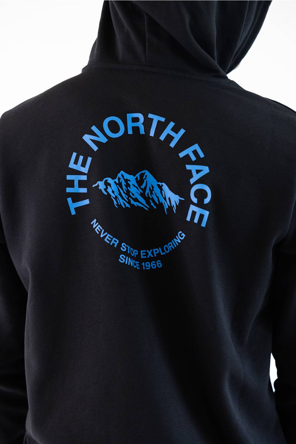 Close-up of the back of a black hoodie featuring a blue graphic print of a mountain range with the text 'THE NORTH FACE' and 'NEVER STOP EXPLORING SINCE 1966'.