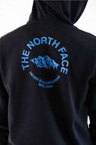 Close-up of the back of a black hoodie featuring a blue graphic print of a mountain range with the text 'THE NORTH FACE' and 'NEVER STOP EXPLORING SINCE 1966'.