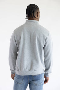 A man viewed from behind wearing a light gray heathered quarter-zip sweatshirt and blue jeans against a plain white studio background.