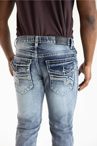 Rear view of a person wearing light-wash blue denim jeans with decorative contrast stitching and zigzag embroidery on the back pockets, paired with a dark brown shirt against a white background.