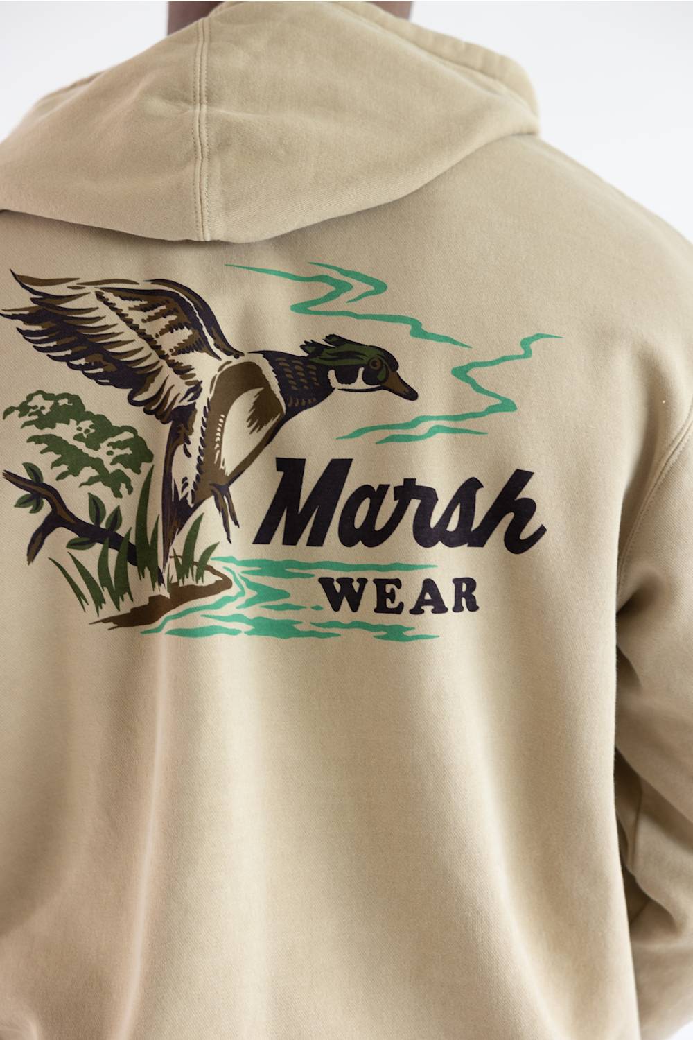 Close-up of the back of a beige hooded sweatshirt featuring a large graphic print of a flying duck, green water and reeds, and the text 'Marsh Wear'.