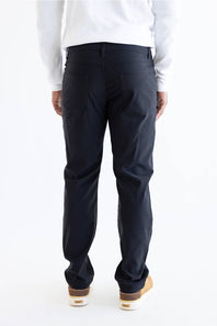 Rear view of a person wearing dark navy pants, a white long-sleeve top, and tan-and-white sneakers against a plain white studio background.