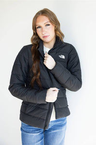 A woman wearing a black puffer jacket by The North Face, styled with a white t-shirt and blue jeans, standing against a plain white background.
