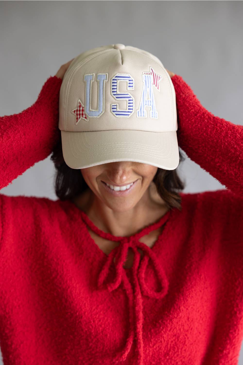 Woman wearing a beige cap with 'USA' and red sweater against a gray background