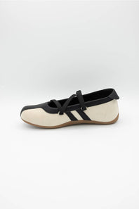 A single women's Mary Jane flat shoe in off-white and black, featuring a black strap with a silver buckle and three black stripes on the side, set against a plain light gray background.