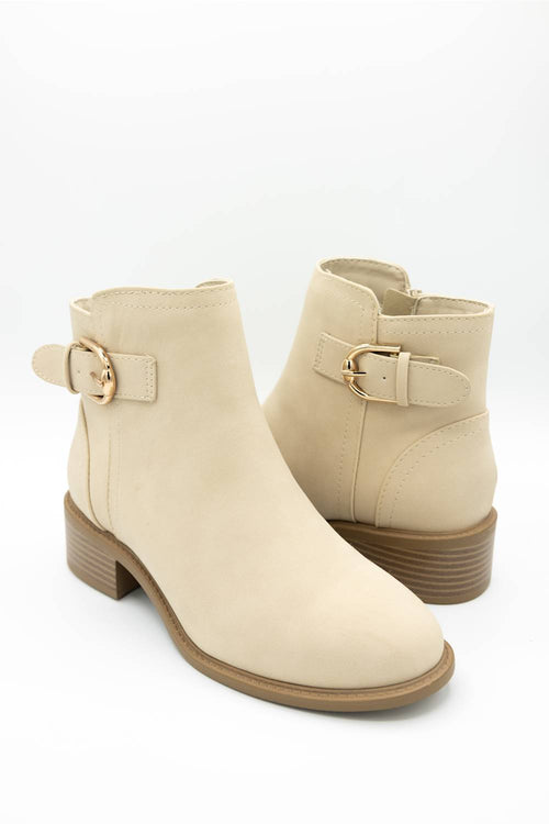 A pair of beige ankle boots with a low block heel and a decorative strap with a gold buckle on the outer side, shown against a plain white background.
