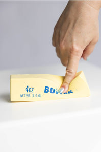 Hand holding a squishy butter toy against a gray background