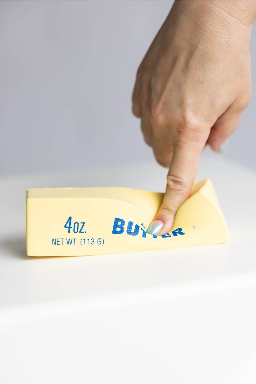 Hand holding a squishy butter toy against a gray background