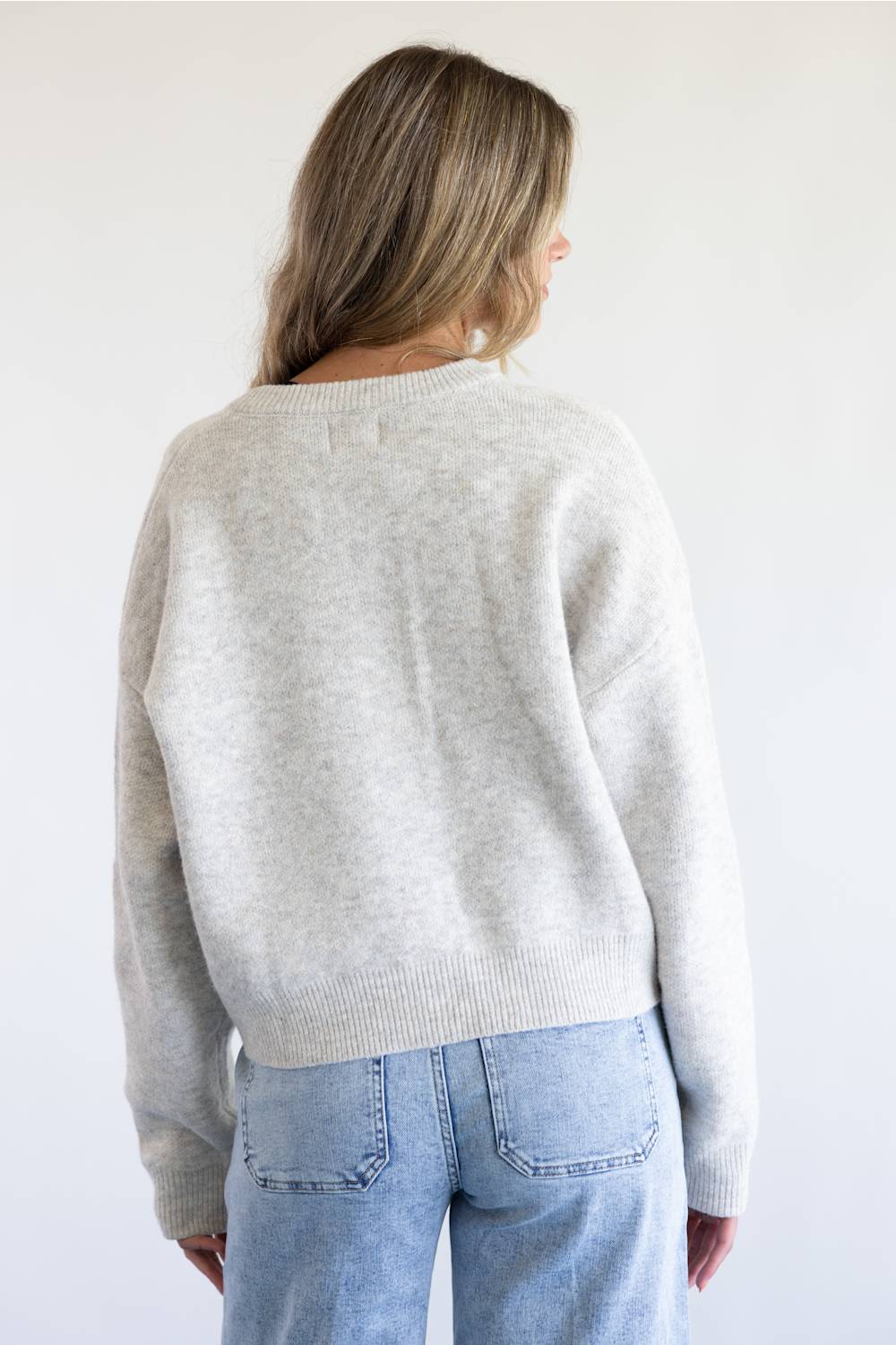 A woman modeling a light gray knit cardigan plain white background.