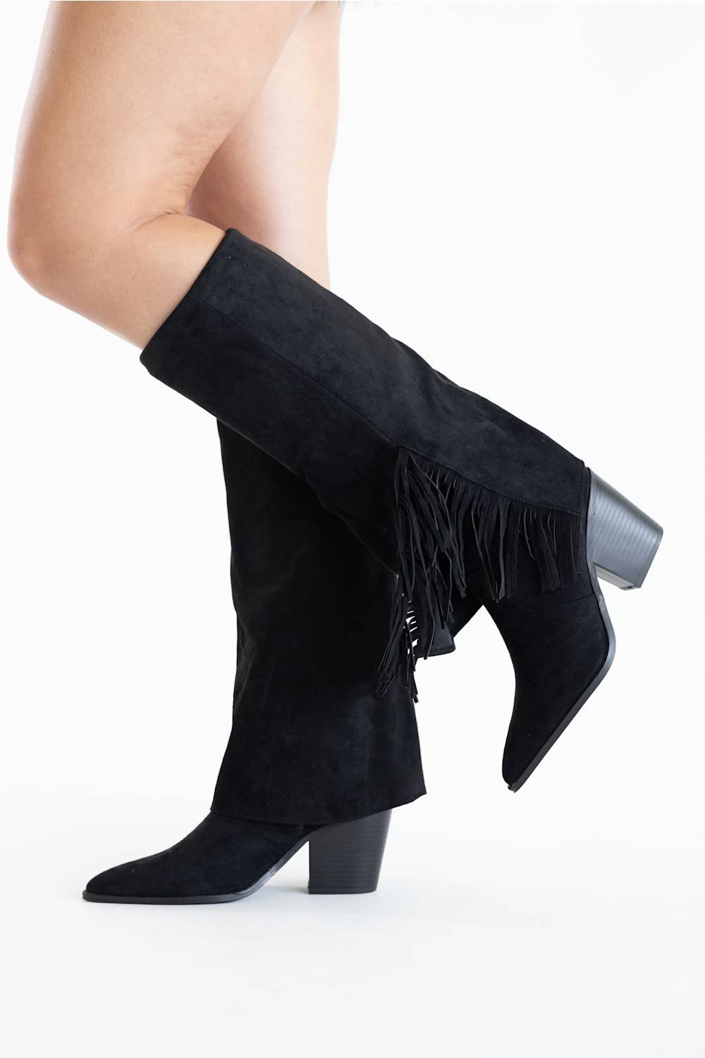 Black suede knee-high boots with fringe detailing and a block heel, shown on a model's legs against a white studio background.