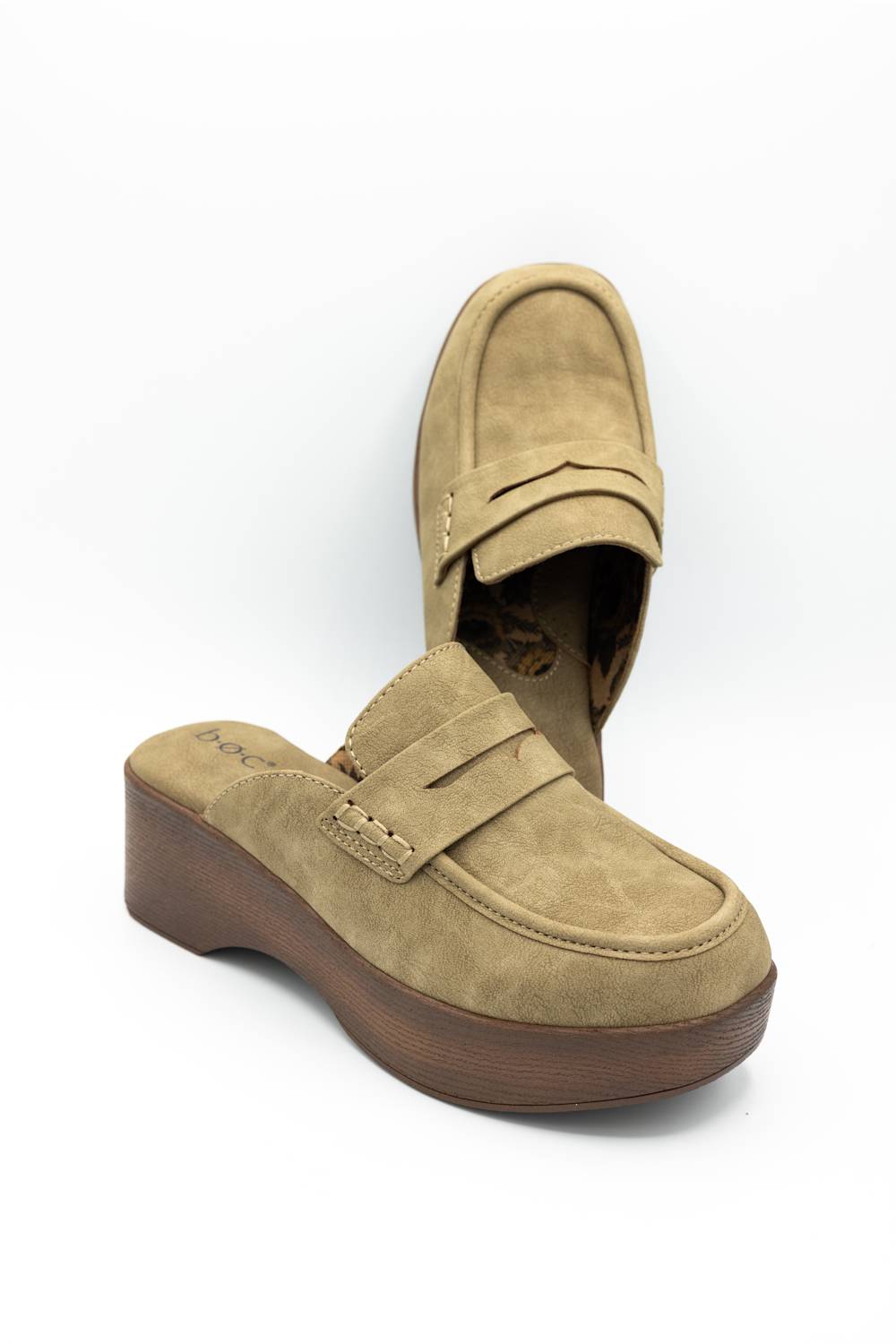 A pair of tan suede slip-on wedge mules with a penny strap, shown on a clean white background.