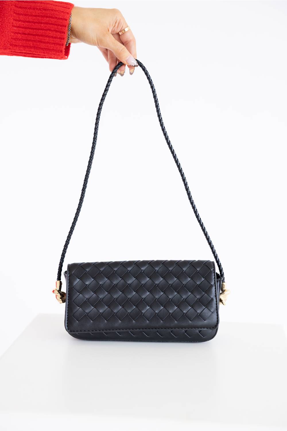 A black woven leather shoulder bag with a braided strap, held by a hand wearing a red sleeve against a clean white background.
