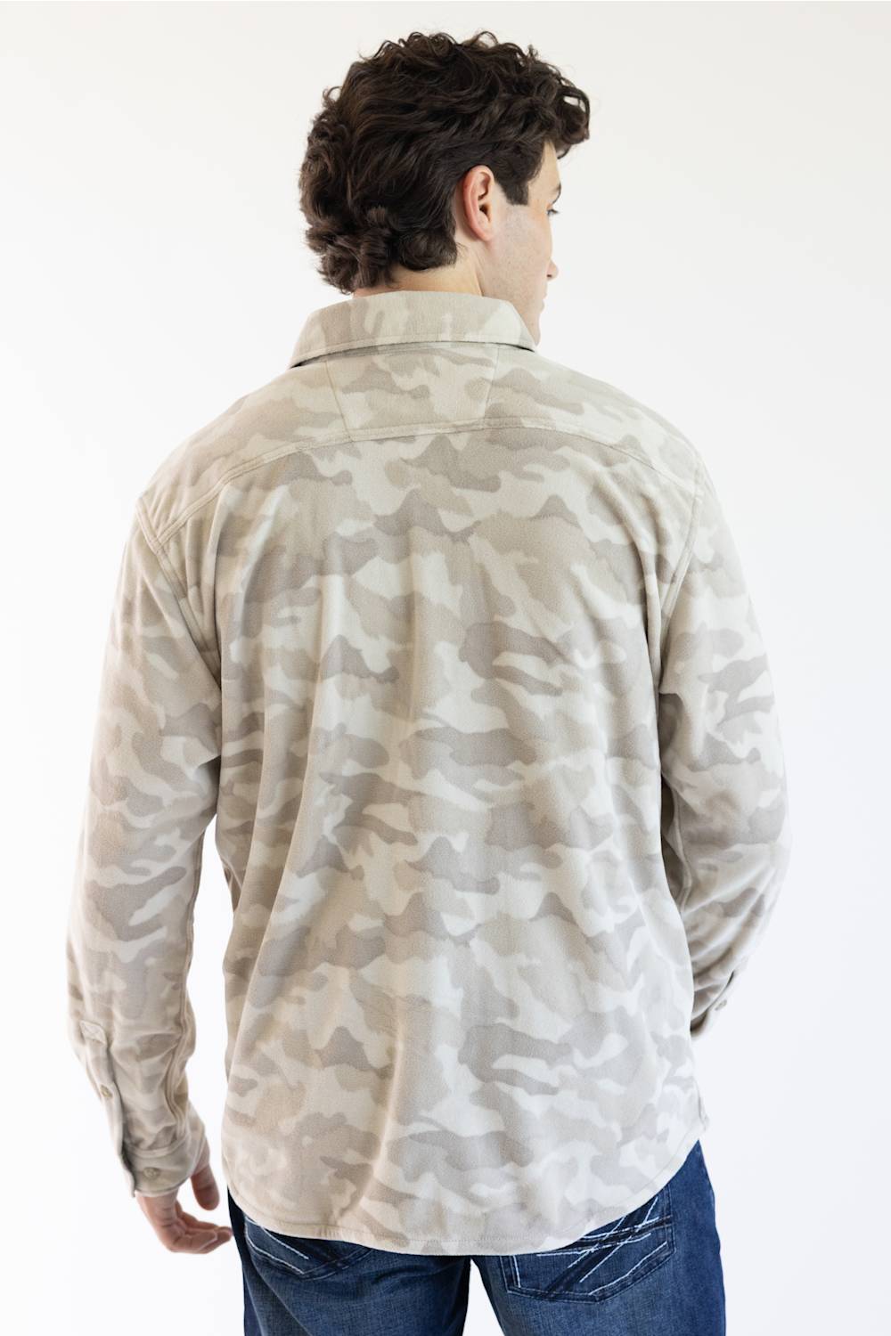 A man viewed from behind wearing a long-sleeve button-up shirt with a beige and gray camouflage pattern, paired with blue jeans, against a plain white background.
