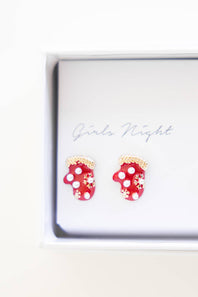 A pair of red mitten-shaped stud earrings with white polka dots and white snowflake details, displayed inside a white gift box with 'Girls Night' written on the insert.