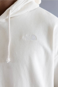 Close-up of a person wearing a white hoodie with a tonal embroidered logo of The North Face on the chest.