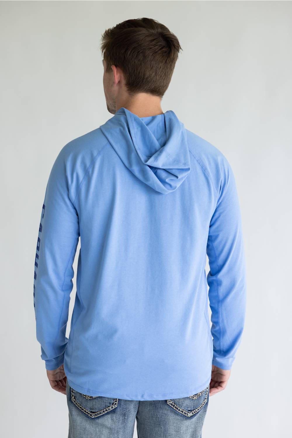 A man viewed from behind wearing a light blue long-sleeve hooded shirt and blue jeans against a plain light gray background.