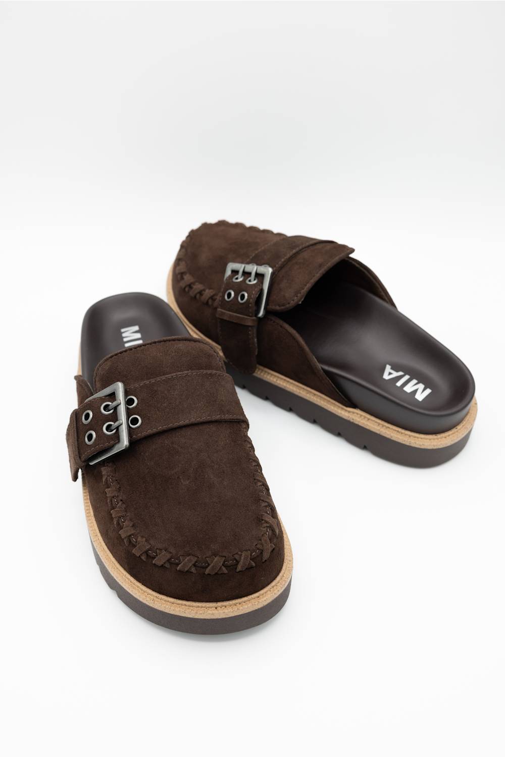 A pair of dark brown suede slide sandals with braided trim and silver-tone buckle straps, displayed on a clean white background.