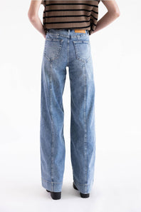 Mica High Rise Wide Trouser Jeans viewed from the back, showing patch pockets, back yoke details, and vertical seams running down the legs. The model is wearing a brown and black striped knit top against a clean white background.