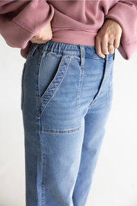 A close-up of a person wearing light blue denim jeans with a pink ribbed sweatshirt, standing against a plain light background.