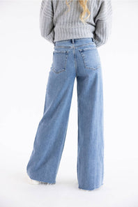 Back view of a woman modeling jeans, with leg popped out