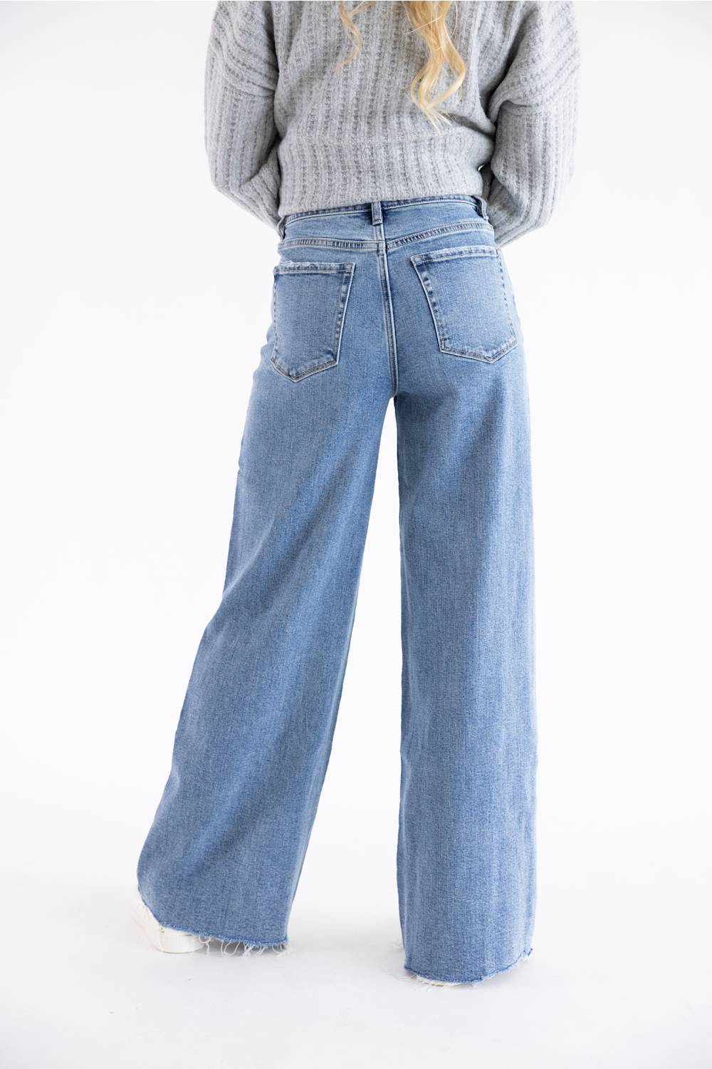 Back view of a woman modeling jeans, with leg popped out