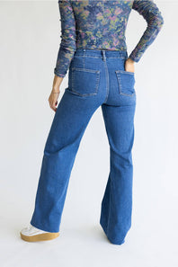 A person shown from the back wearing blue wide-leg jeans, a floral long-sleeve top, and white sneakers against a plain light background.