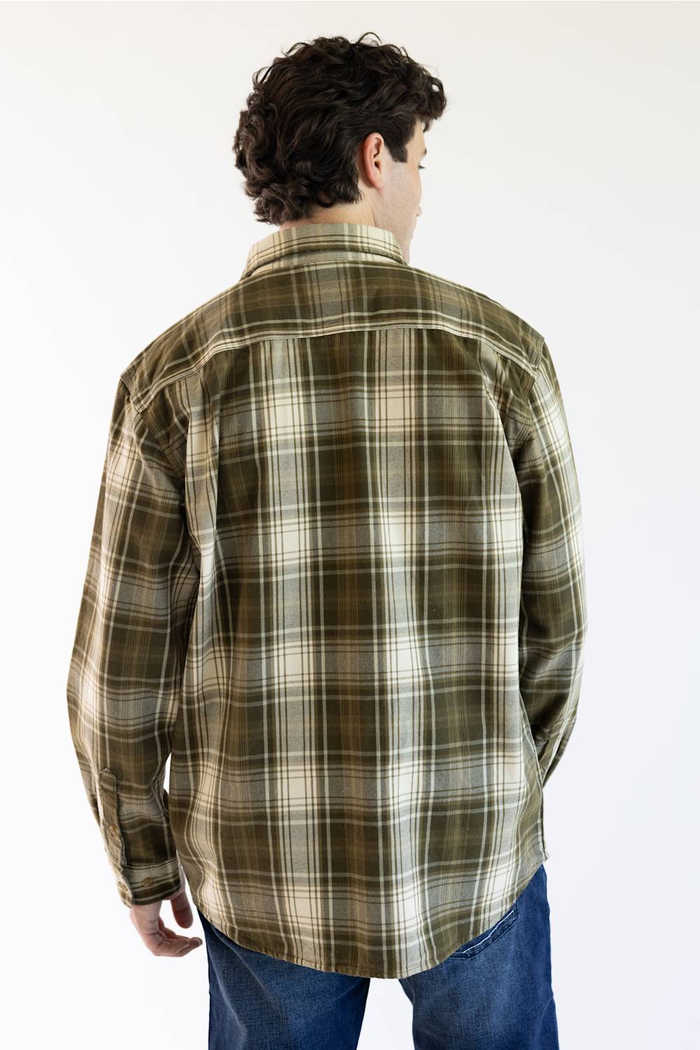 A man viewed from behind wearing a long-sleeve plaid flannel shirt in olive green, brown, and cream, paired with blue jeans, against a plain white background.