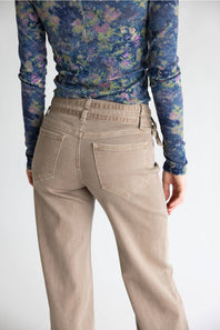 A person shown from the back wearing beige straight-leg jeans and a blue floral long-sleeve top against a plain light gray background.