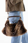 A brown faux fur shoulder bag with a dark brown leather strap and gold-tone hardware, shown being worn over the shoulder of a person wearing blue jeans and an olive green jacket.