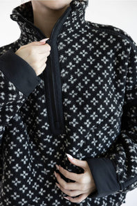 Close-up of a person wearing a black and white patterned fleece half-zip jacket, pulling the zipper with one hand.