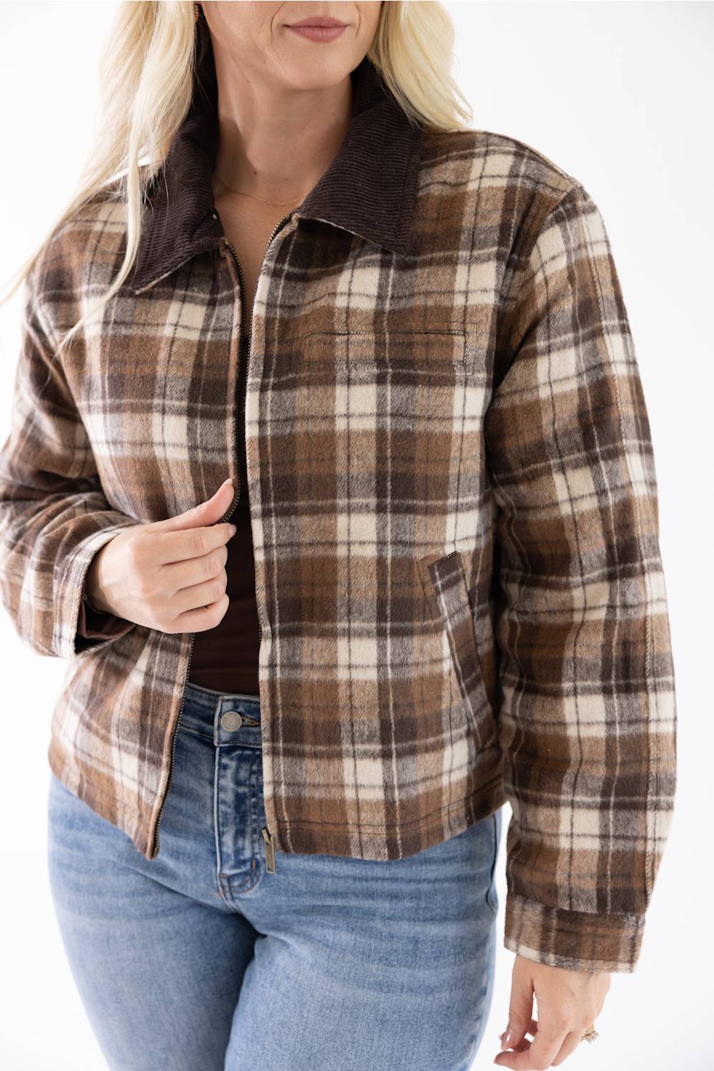 Model wearing the Brown and Cream Plaid Barn Jacket with a dark brown corduroy collar, unzipped to reveal a brown top, paired with blue jeans and holding the front edge of the jacket.