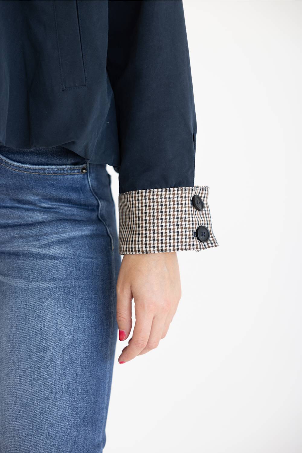 Close-up of a person wearing a dark navy long-sleeve top with a black-and-white gingham buttoned cuff, paired with blue jeans against a plain white background.